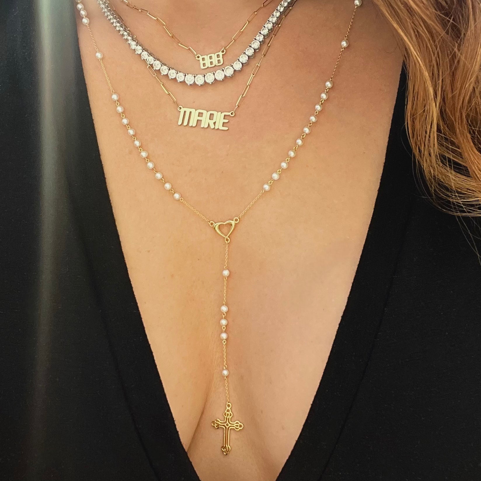 Pearl rosary necklace with gold heart centerpiece worn with a graduated tennis necklace, a gold nameplate necklace, and an 888 angel number necklace