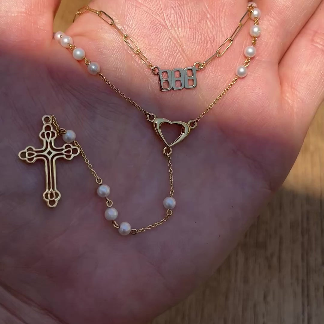 Closeup of our Paloma pearl rosary necklace with gold open heart centerpiece and cross, with an angel number 888 necklace