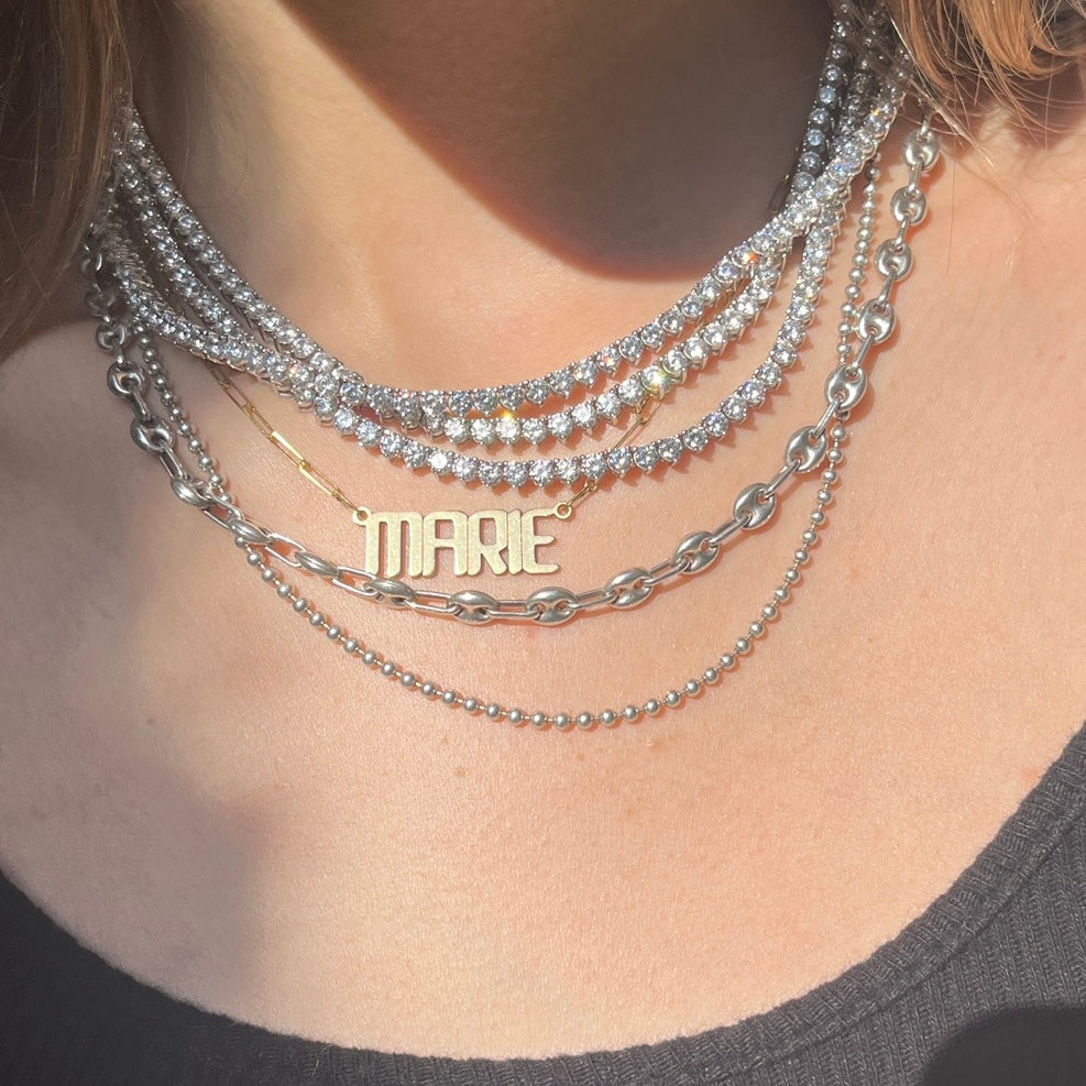Our custom nameplate necklace in 14k gold with name Marie, styled with tennis necklaces and chains