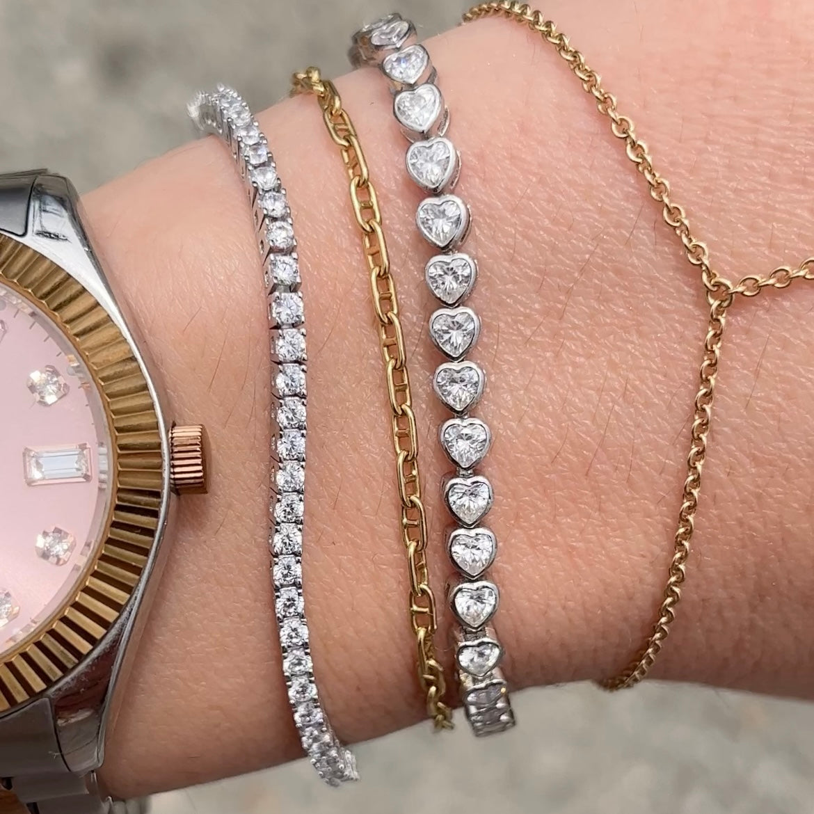 Closeup of our sterling silver 4 prong 2mm thin tennis bracelet on a wrist with other bracelets