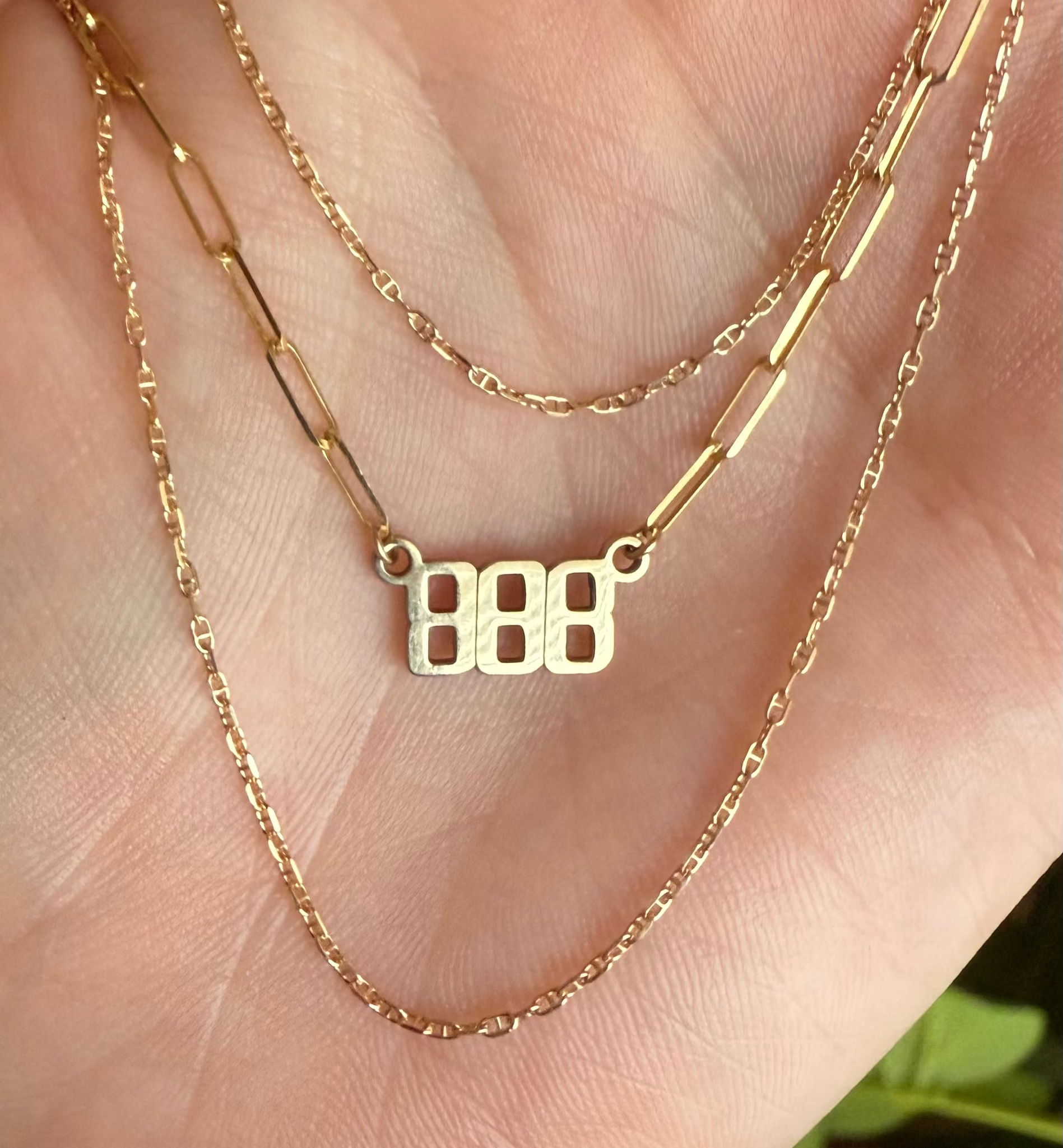 Gold necklace with '888' pendant on a hand