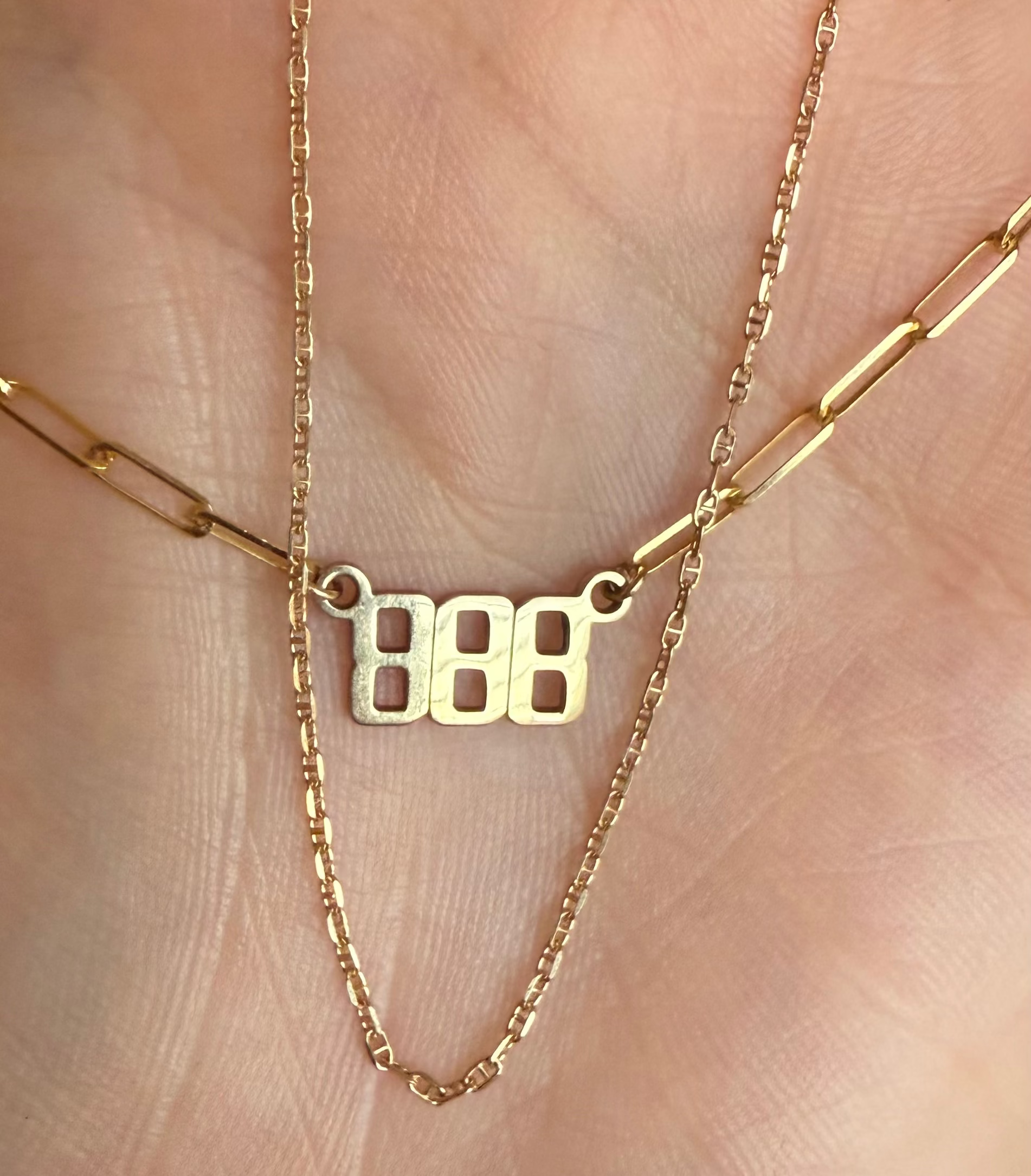 Gold necklace with a '888' pendant on a hand