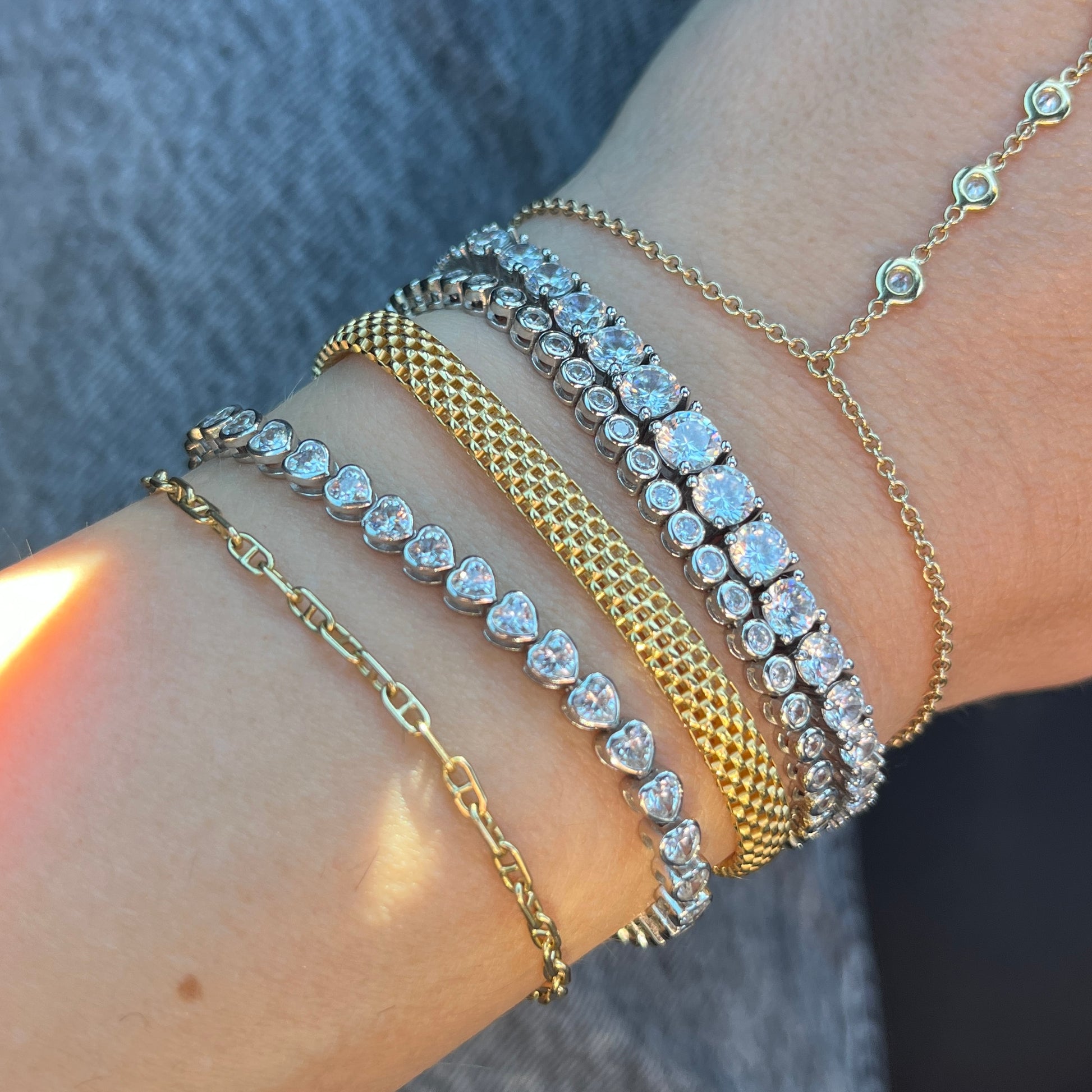 Three faux tennis bracelets mixe with yellow gold bracelets show on a wrist