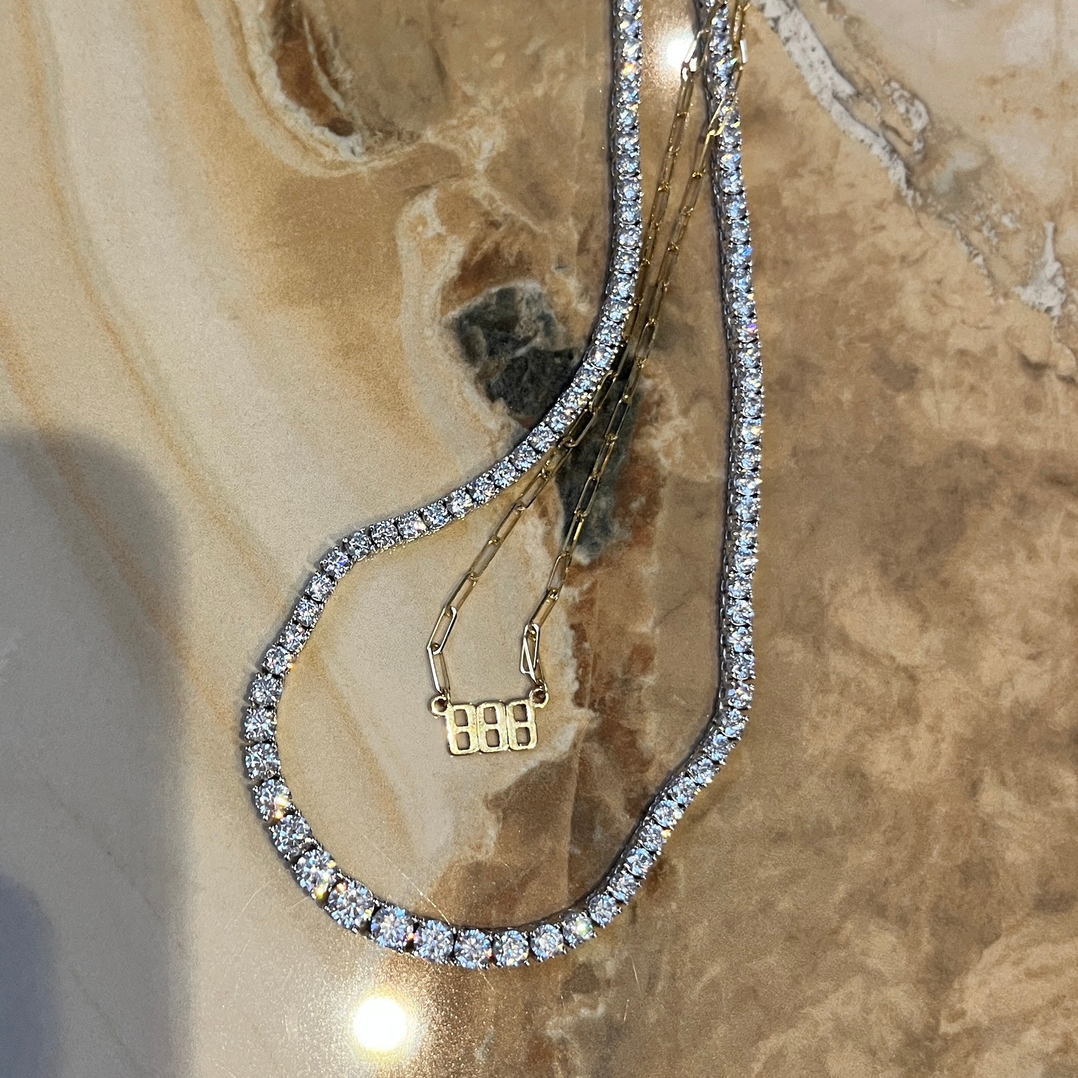 Graduated faux tennis necklace on a marble surface with an angel number 888 nameplate necklace 