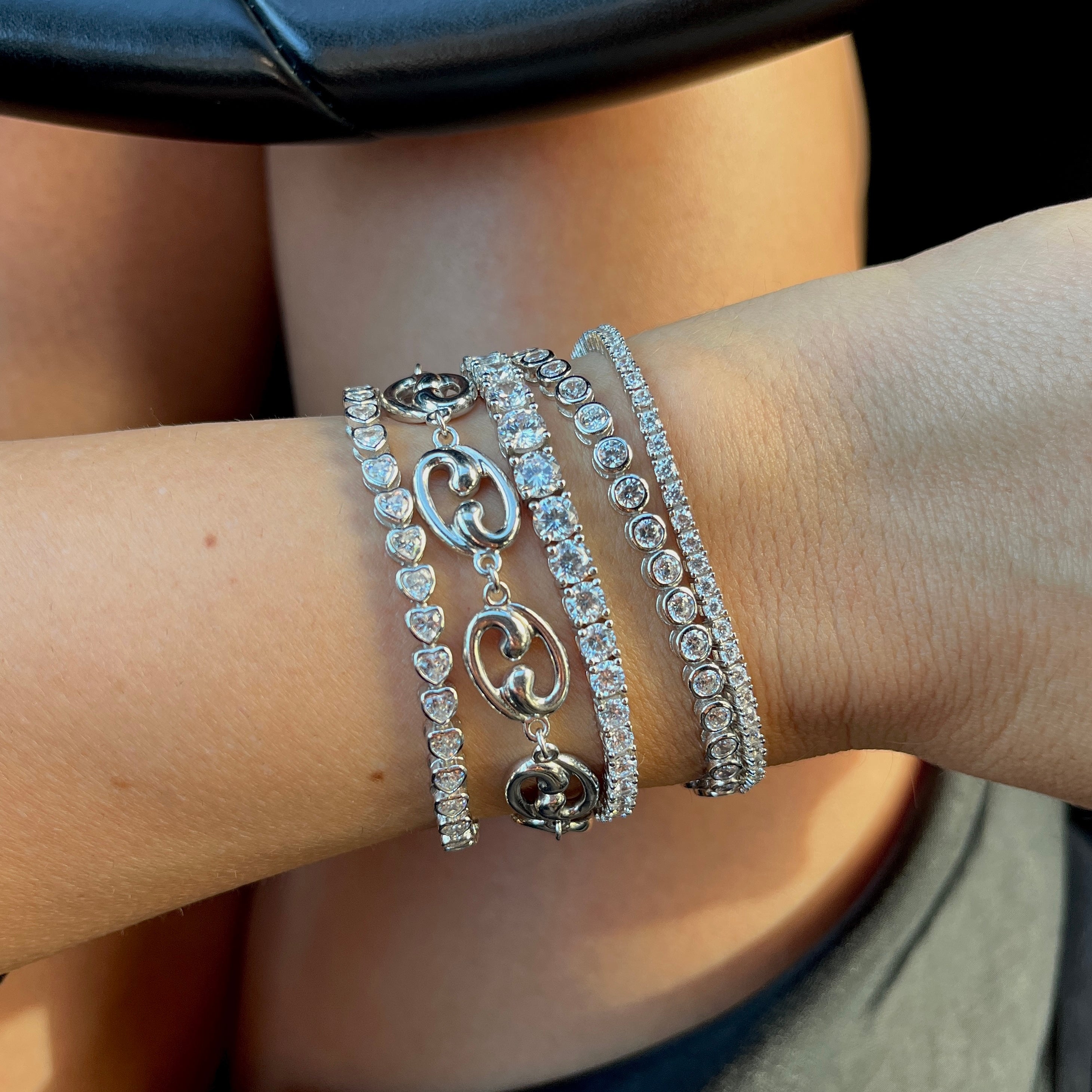 Stack of tennis bracelet on a wrist with a Fibonacci link bracelet in silver, a graduated tennis bracelet, a thin tennis bracelet, and bezel tennis bracelets by Leni James