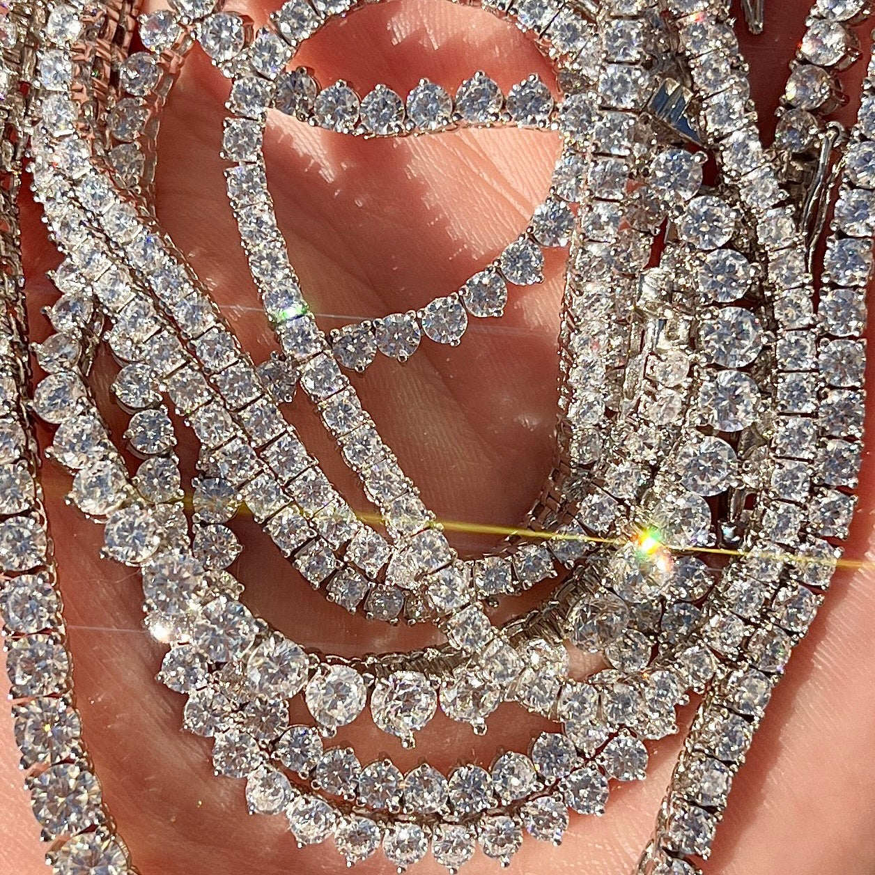 Close-up of a stack of sparkling diamond tennis necklaces on a hand