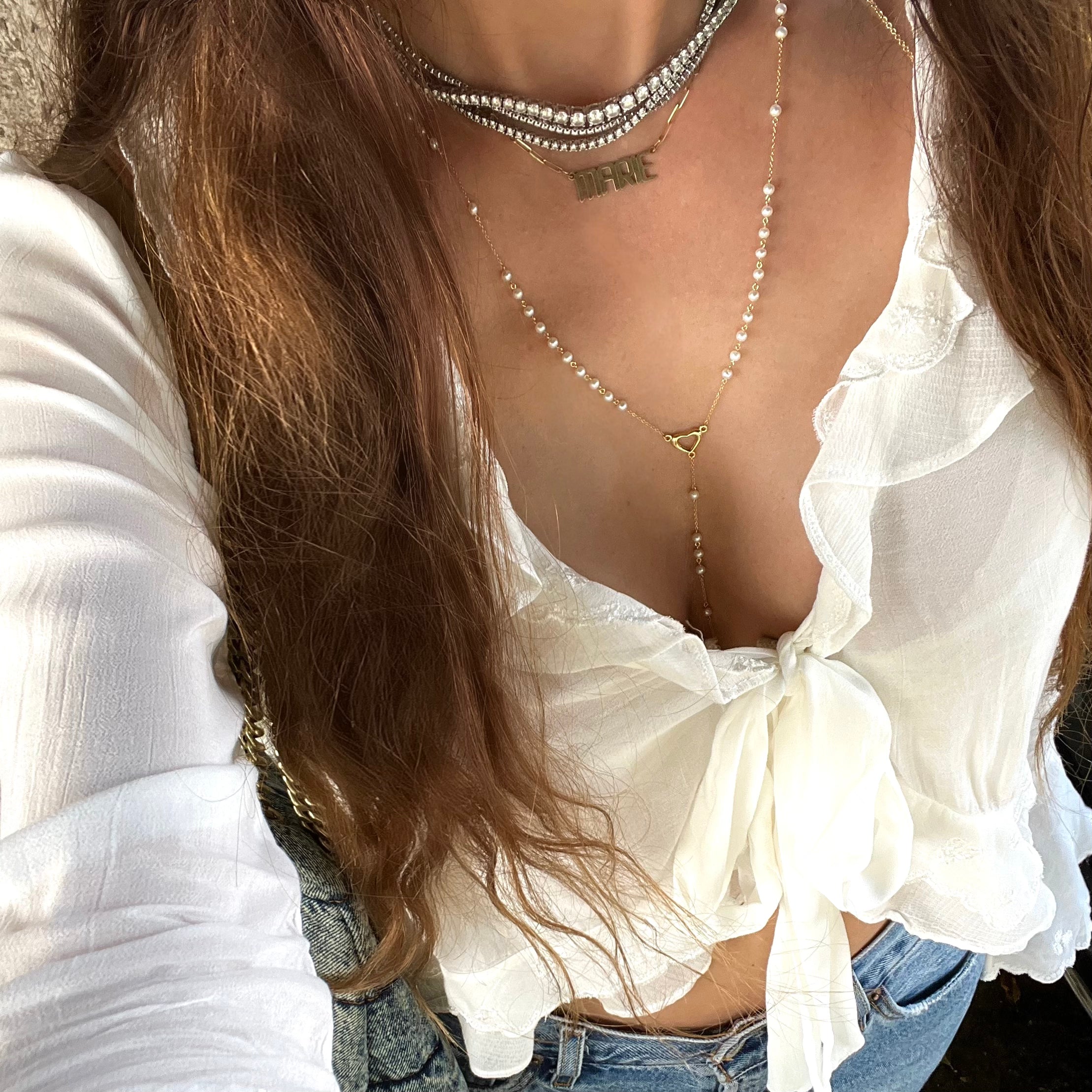 Pearl rosary necklace with gold open heart, nameplate necklace, and three tennis necklaces stacked and layered 