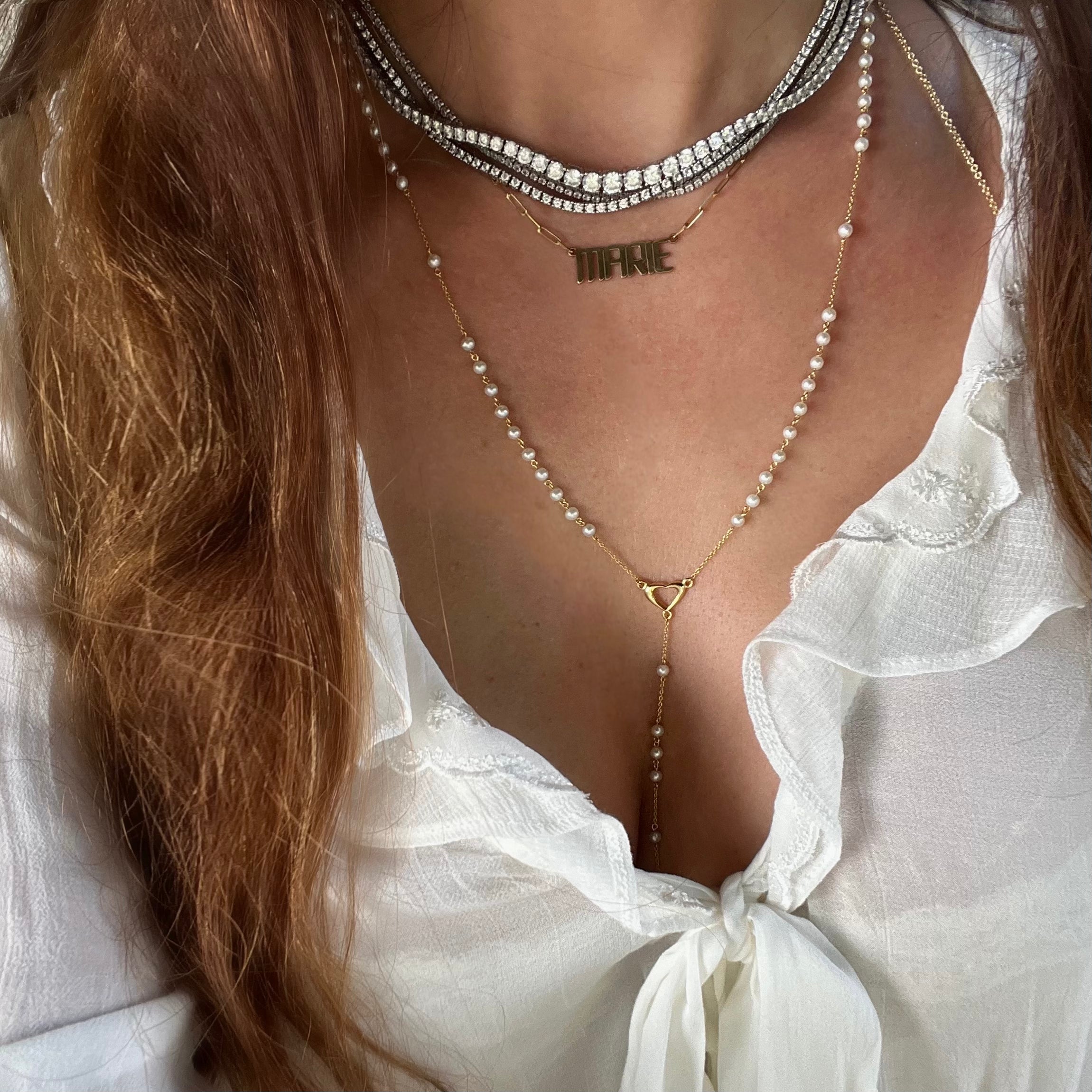 Closeup of our Paloma pearl rosary necklace with a gold heart, nameplate necklace, and tennis necklaces layered