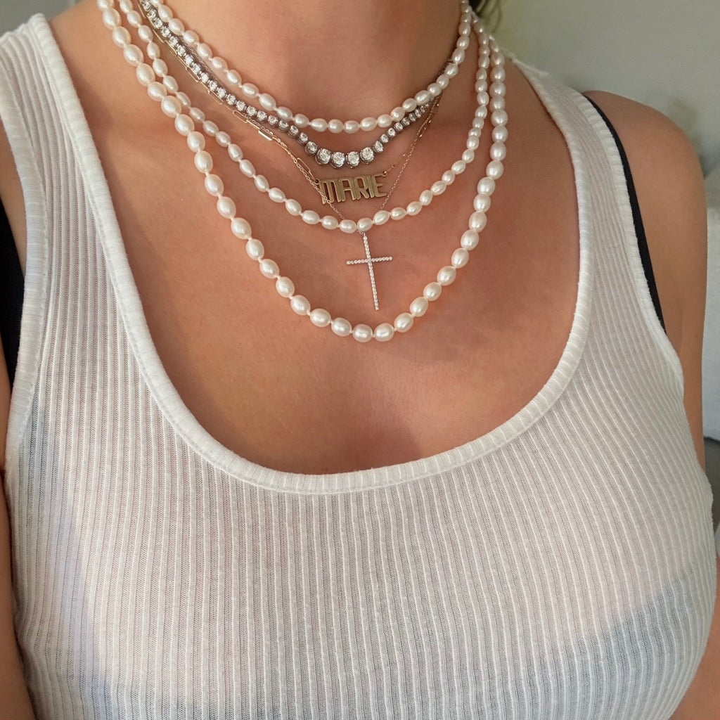 Pearl necklaces layered with a tennis necklace, a pave cross pendant , and a gold nameplate necklace 