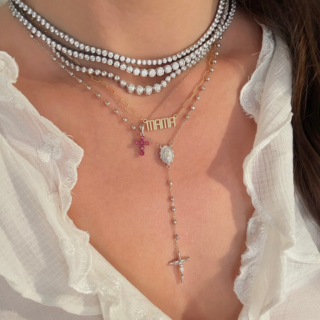 Layered tennis necklaces styled with a ruby cross, a gold Mama nameplate necklace and a sterling silver rosary