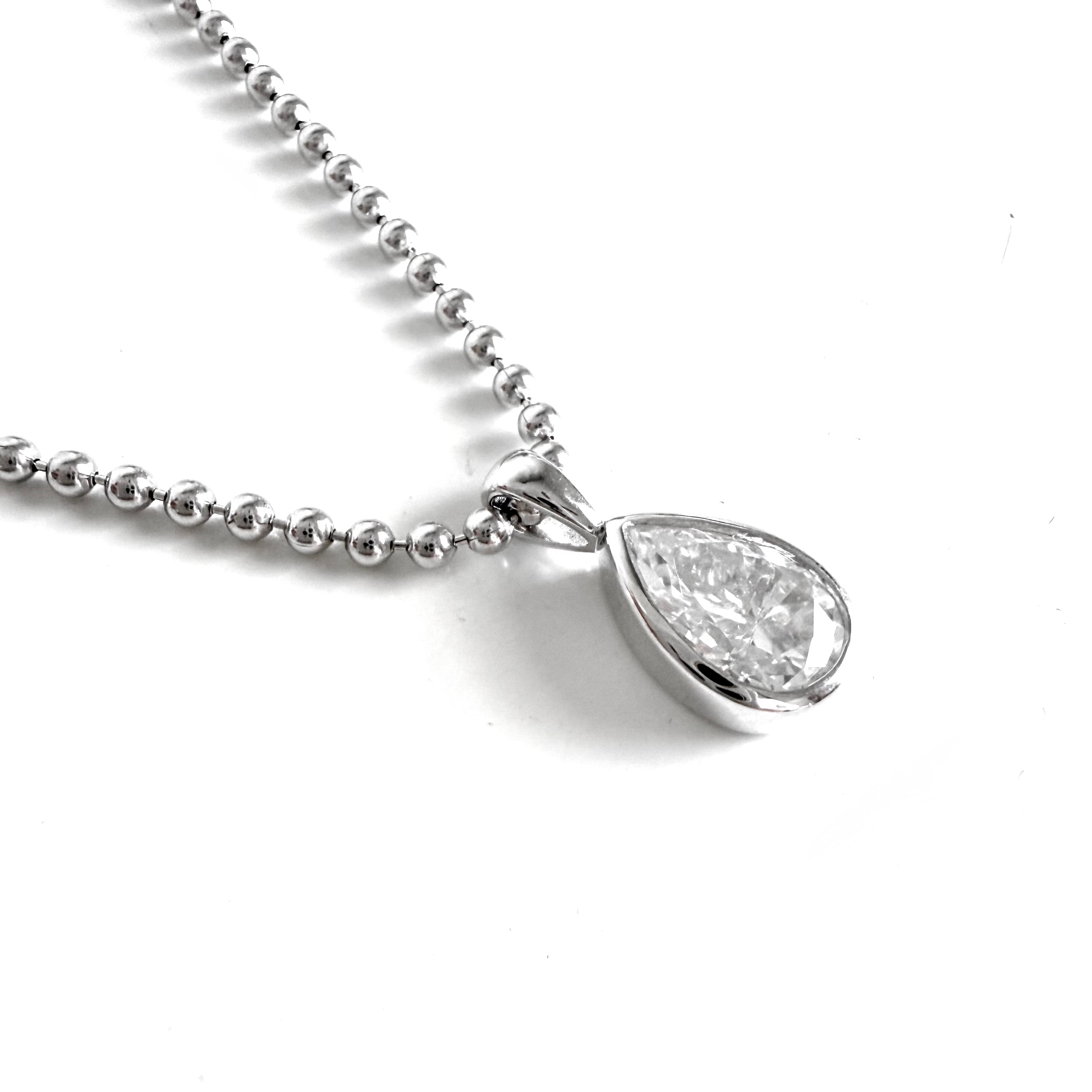 A silver ball chain necklace with a teardrop-shaped moissanite pendant in a sterling silver bezel setting