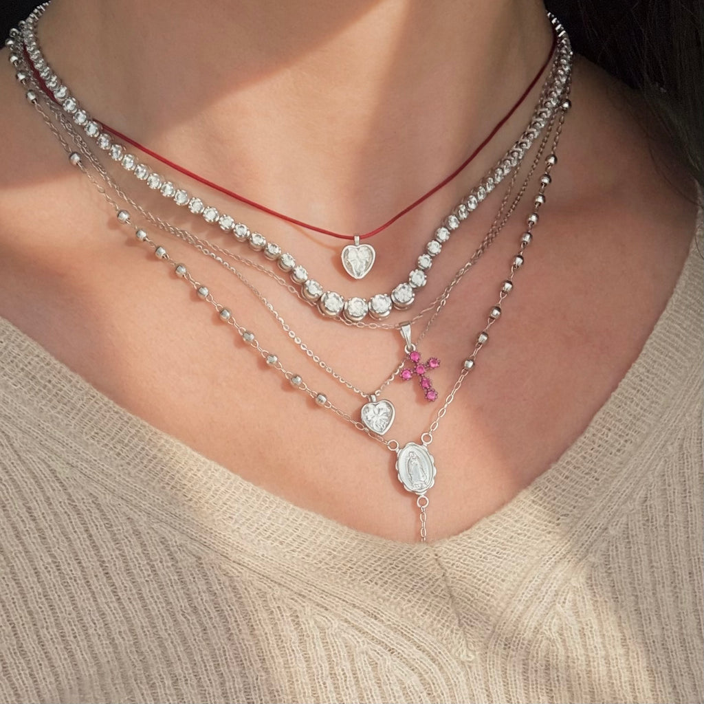 Pink cross pendant layered with heart bezel necklaces and a tennis necklace