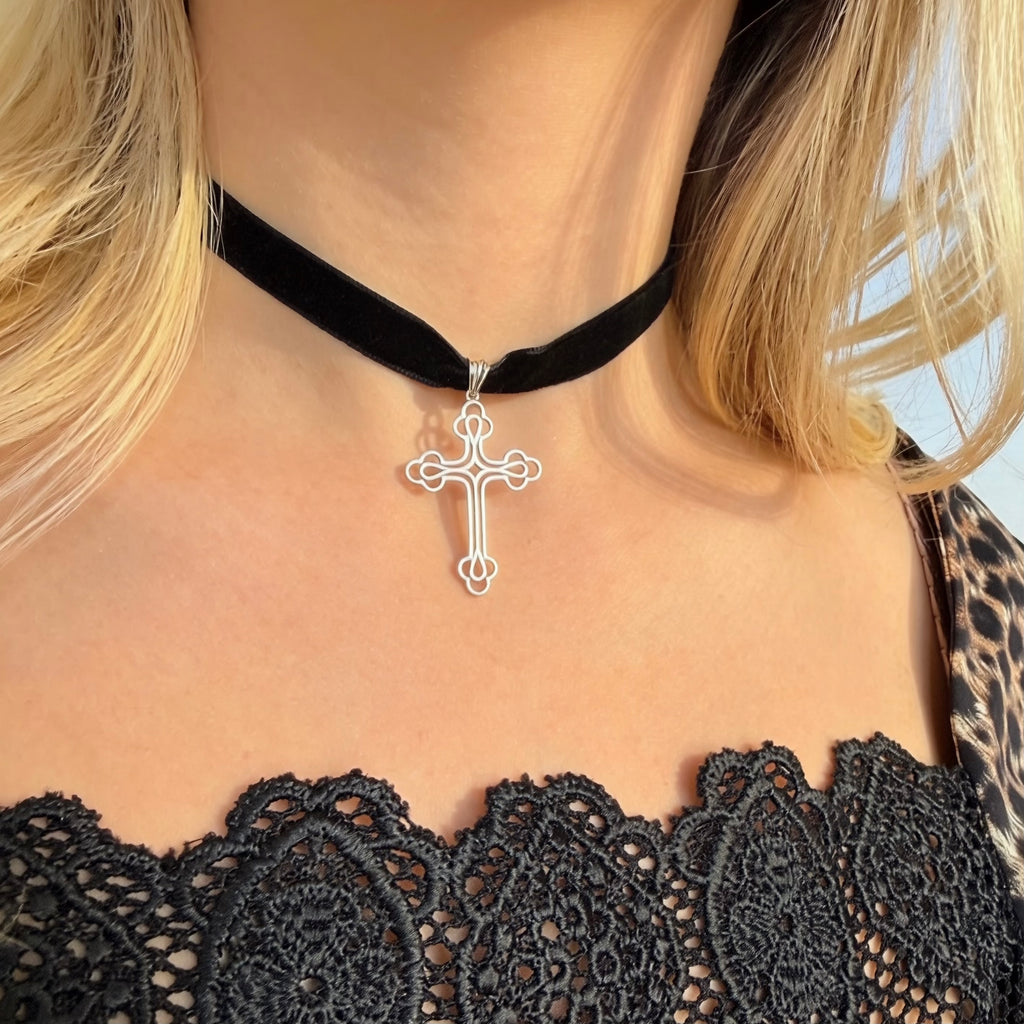 Black velvet choker with a silver cross pendant worn by a person with blonde hair.