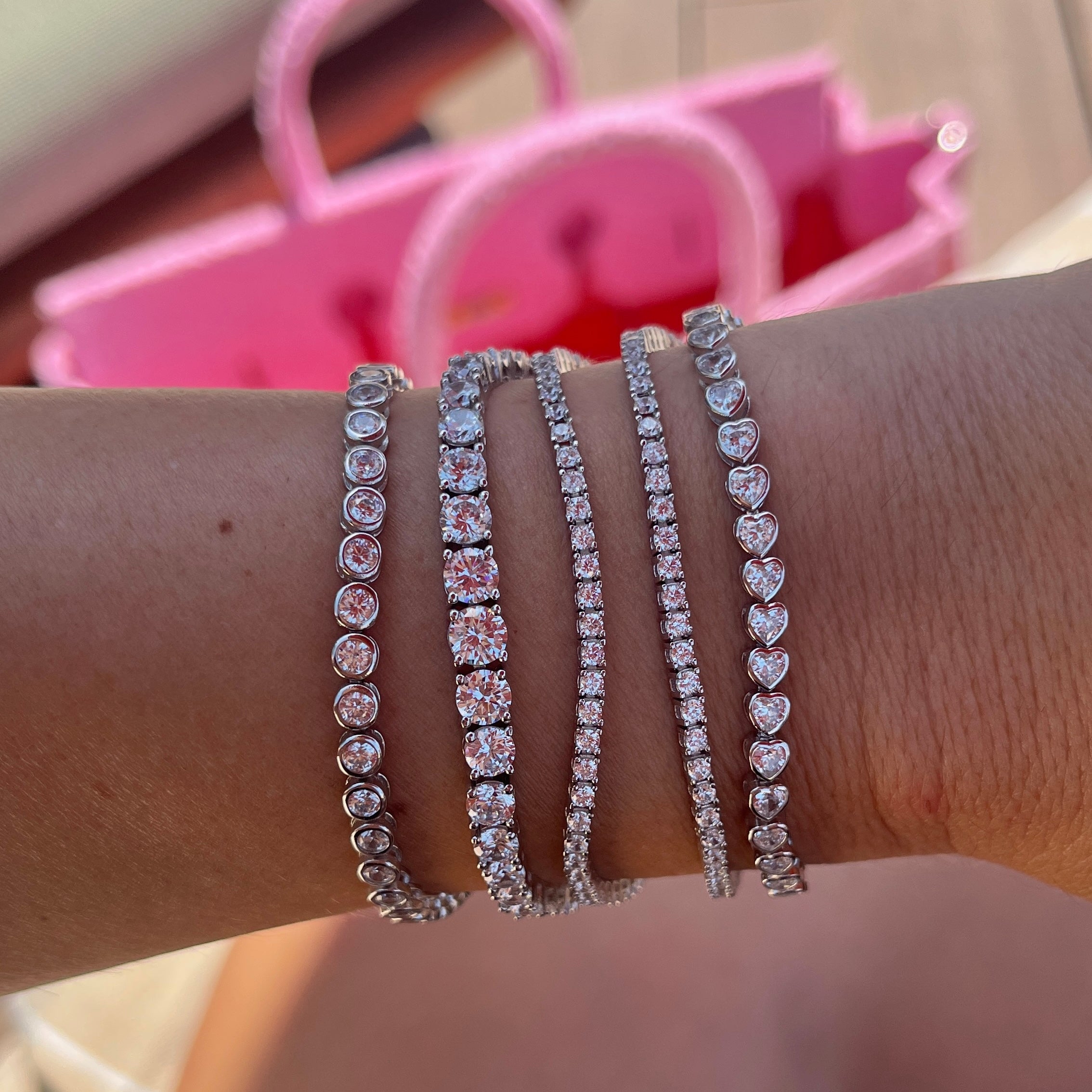 Stack of five Leni James tennis bracelets on a wrist with thin tennis bracelets, a graduated tennis bracelet, and a heart bezel tennis bracelet 