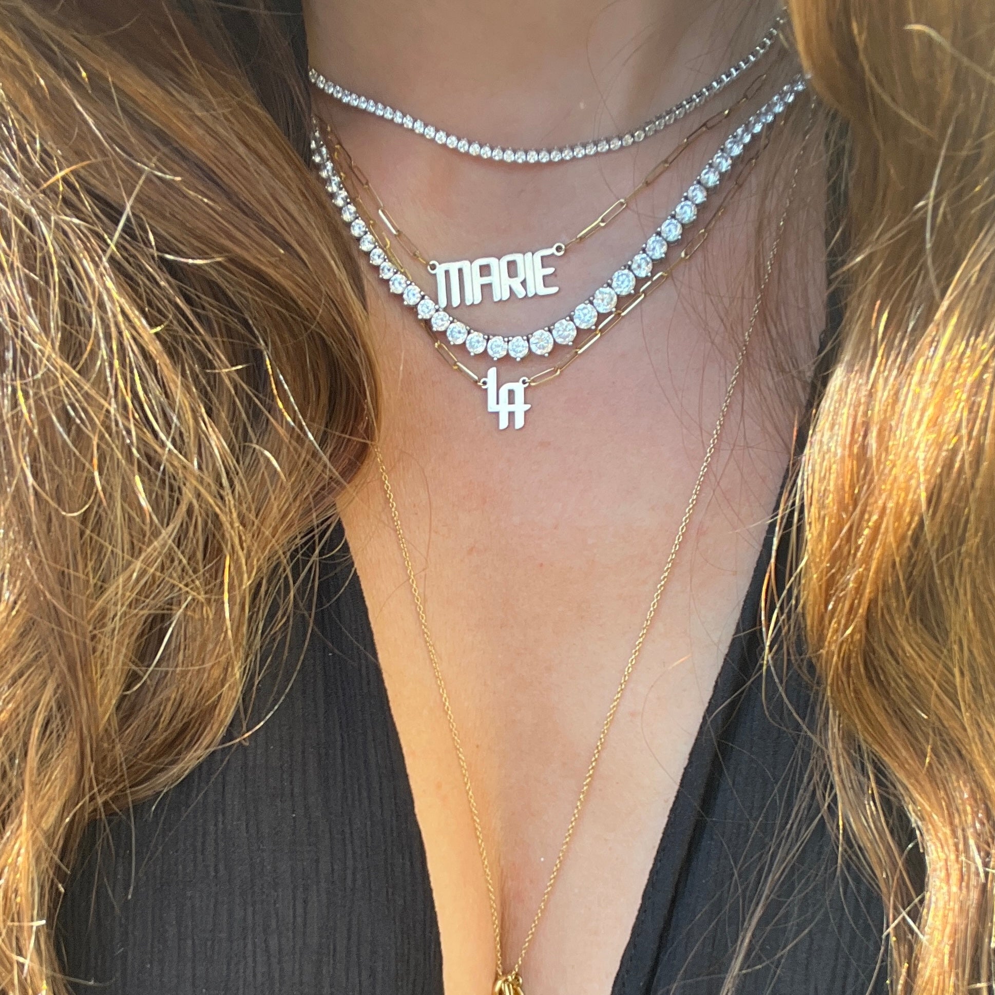 a thin tennis necklace and a graduated tennis necklace with gold nameplate necklaces
