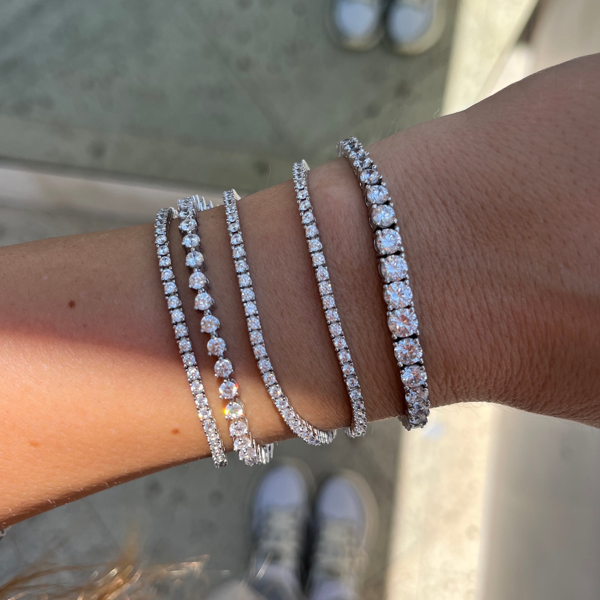 Close up of thin tennis bracelets on a wrist, with also a graduated tennis bracelet and a silver 3 prong tennis bracelet