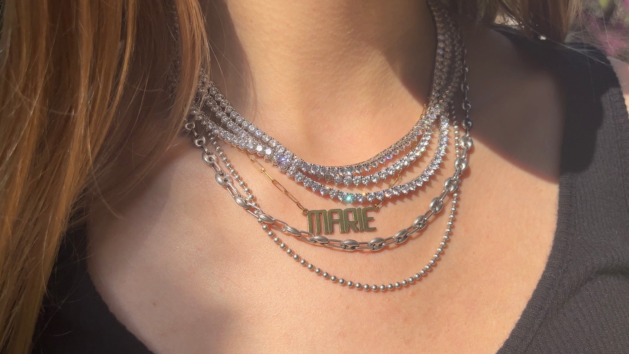 Our lab diamond tennis necklace shown on neck with chains and our custom nameplate necklace